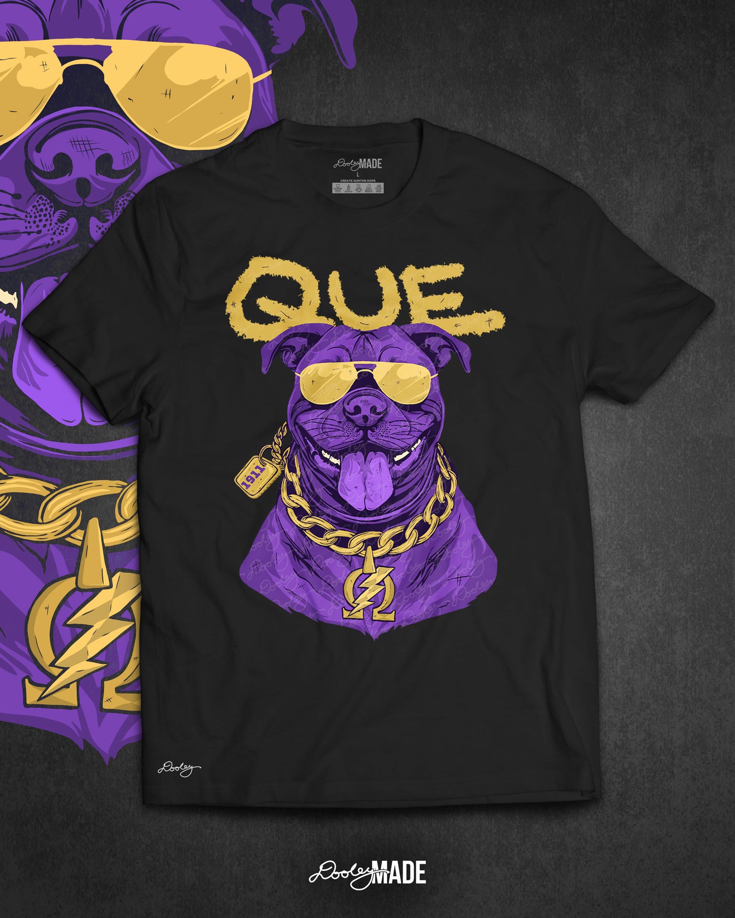 A photo of a black shirt with a graphic of an Omega Psi Phi themed Pit Bull Dog wearing gold aviator sunglasses and a gold Omega Psi Phi necklace.