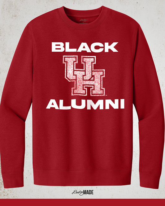 Image of a red "Black UH Alumni Crewneck Sweatshirt" with bold, white text reading "BLACK ALUMNI" surrounding a speckled red "UH" logo in the center. The design highlights pride and unity for Black Alumni of the University of Houston, presented on a modern and stylish garment perfect for showing school spirit.