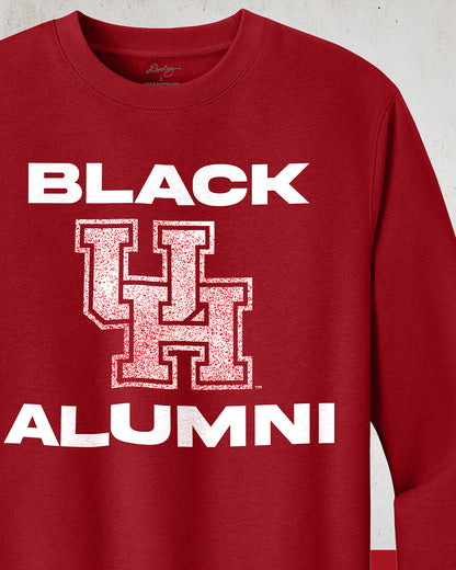 Image of a red "Black UH Alumni Crewneck Sweatshirt" with bold, white text reading "BLACK ALUMNI" surrounding a speckled red "UH" logo in the center. The design highlights pride and unity for Black Alumni of the University of Houston, presented on a modern and stylish garment perfect for showing school spirit.