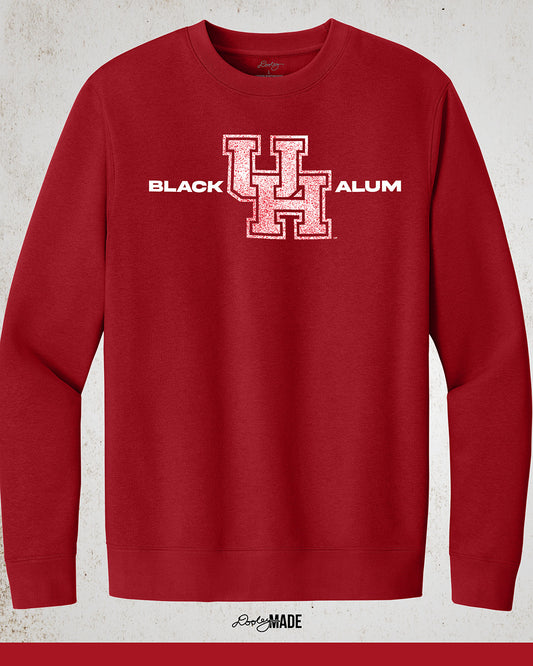 Image of a red "Black UH Alumni Crewneck Sweatshirt" with bold, white text reading "BLACK ALUMNI" surrounding a speckled red "UH" logo in the center. The design highlights pride and unity for Black Alumni of the University of Houston, presented on a modern and stylish garment perfect for showing school spirit.